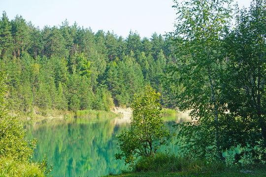 Pine forest is reflected in the surface of the green-blue water of the chalk pits in the center of Belarus, Lyuban