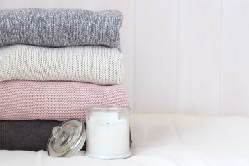 Obraz na płótnie Canvas stack of knitted sweaters on a wooden wall background. Scented candles. Cozy warm, rustic-style winter clothes. Stylish casual woolen autumn wardrobe. Hyugge Lagom concept copy space