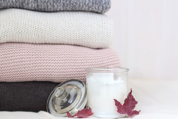 Obraz na płótnie Canvas Stack of knitted sweaters on wooden wall background. Scented candle and fallen maple leaves. Cozy warm, rustic-style winter clothes. Stylish daily casual woolen autumn wardrobe. Hyugge Lagom concept. 