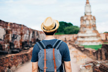 Back of Asian male solo traveller with travel hat walks inside historical buddhist ruins heritage with ancient temples in background in Ayutthaya, Thailand