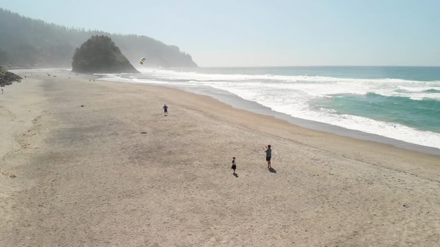 Aerial footage of the beach and rocky cliffs of the Oregon coast near Lincoln City with a child flying a kite in the foreground.