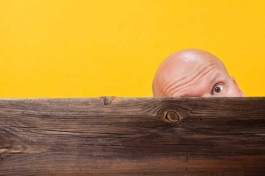 Shaved Head Protrudes Behind An Old Board On A Yellow Background