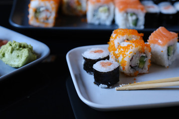 Sushi roll with seafood and soy sauce, wasabi and ginger. Sushi roll with salmon and flying fish caviar on a black table