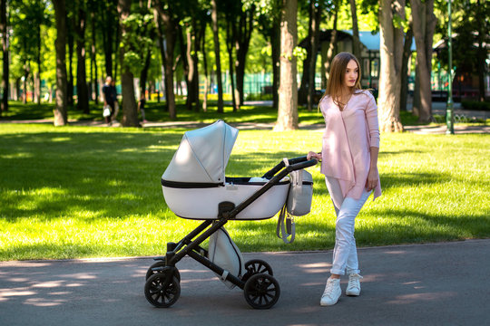 Young Mom Walks With Stroller In The Park