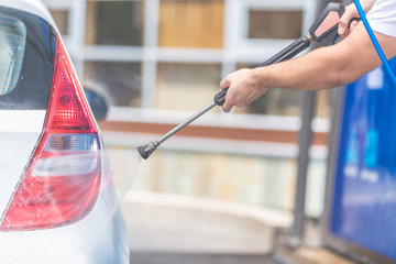 Close up of man washing rear part of the car under high pressure water outdoors.