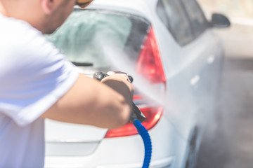 Rear lights and trunk washing with pressurized water in car wash outdoors.