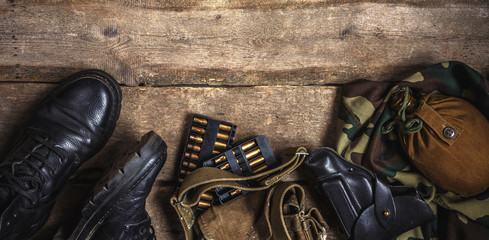 Army military uniform, weapon, holster, pistol, flask, boots on wooden background. Flat lay top...