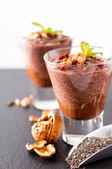 Healthy food concept Chia seeds, chocolate milk pudding with goji and dried walnuts in small Glass on black slate board background