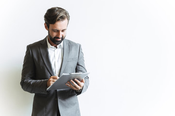 Image of handsome successful businessman holding clipboard and writing down notes while working in...