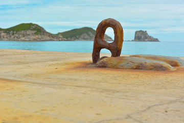 Large rusty noose on a concrete pier, turquoise sea and green islands on the horizon