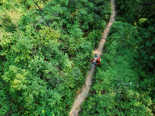 Aerail view of cross country biking woman cyclist with mountain bike walking on tropical rainforest trail