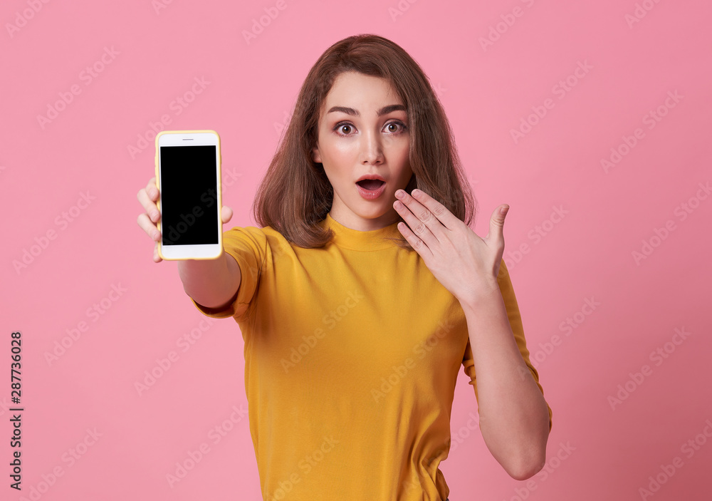 Poster Portrait of a excited young woman showing at blank screen mobile phone isolated over pink background.