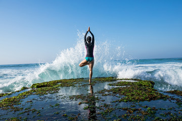 Yoga woman meditation at the seaside cliff edge facing the coming strong sea waves