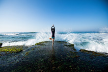 Yoga woman meditation at the seaside cliff edge facing the coming strong sea waves