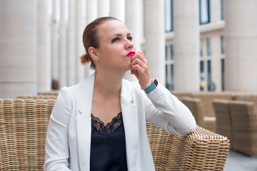 Young pensive contemplative business woman in suit sitting daydreaming or waiting for someone at...