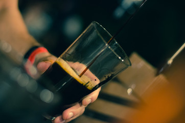 bartender pours dark beer in a glass at the bar