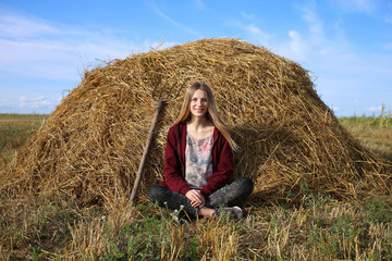Naklejka na ściany i meble Beautiful, blonde girl, with a smile on her face, sits on a hay in the lotus position.