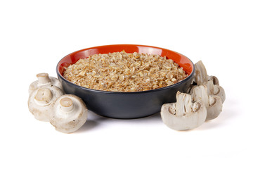 Sprouted wheat porridge in red and black bowl with raw white champignon mushrooms near it. Isolated on white background. Idea for healthy diet meal.