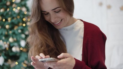 Serious businesswoman searching presents on phone in christmas decorated home