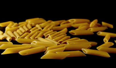 Penne rigate pasta pile isolated on black background