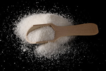 Sugar crystals, pile with wooden spoon isolated on black background