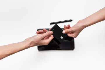 Close up top view of a woman hands over bank card to a man in order to pay for the product. Tablet and pen on a white table. Concept of e-commerce and online shopping. Successful deal.