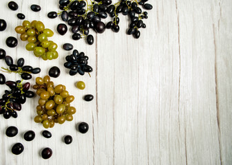 Fresh fruits on a white wooden background. Frame made of prunes, black and green grapes.