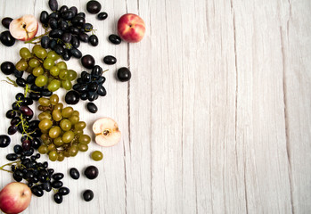 Fresh fruits on a white wooden background. Red apples, prunes, black and green grapes.