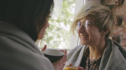 Lesbian couple wrapped in blankets drinking coffee