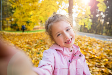 Cute little girl with missing teeth taking selfie. Happy child laughing and smiling. Sunny autumn forest, sun beam. 