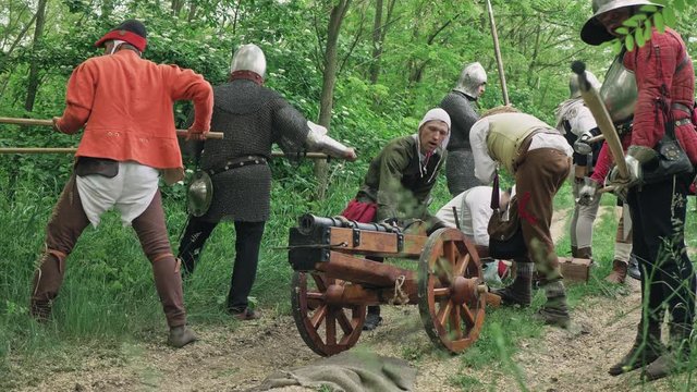 Warriors preparing to the attack and the artilleryist shoot from the cannon on the forest trail.