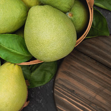Fresh pomelo, grapefruit in bamboo basket with green leaf on dark black slate background. Seasonal fruit for Mid-Autumn Festival. Top view. Flat lay.