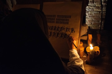 The hands of a medieval monk who write a manuscript by candlelight