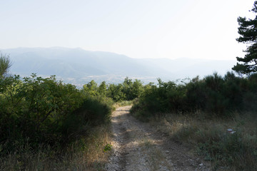 Mountain path that descends towards the valley and fog on the horizon
