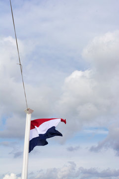 View on the Dutch flag, a triband flag with the colors red white and blue, waving in the wind. A typical dutch sky with clouds and patches of blue.