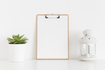 Wooden clipboard mockup with a succulent plant and a candle holder on a white table.