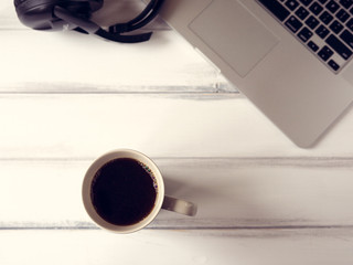 White wooden working desk with notebook, headphones and large mug of coffee. Color toned, shallow depth of field. Topview.