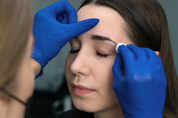 Beautiful young woman gets eyebrow correction procedure. Young woman tweezing her eyebrows in beauty saloon. Master gives shape and thread plucks eyebrows in a beauty salon. Professional care for face