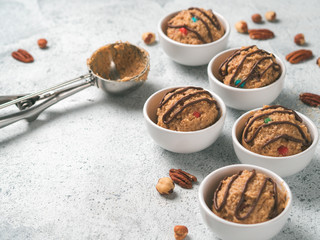 Safe-to-eat raw monster cookie dough in small portion bowl, ice cream scoop and nuts on gray cement background. Ideas and recipes for kids and toddlers meal. Copy space for text.