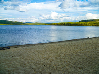 The sandy shore of a forest lake in northern Russia attracts tourists from different places.
