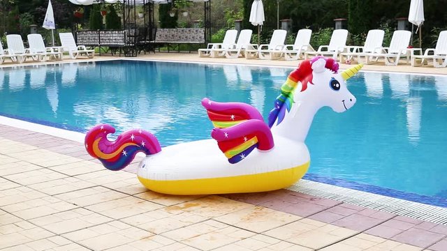Unicorn pool float in blue water background, inflatable swim tube. Pool party, summer holidays, beach vacation.