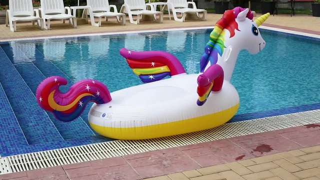 Inflatable unicorn near pool with blue water. Pool party, summer holidays, beach vacation. Fantasy swim ring for summer pool trip.