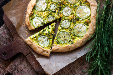 Homemade courgette and goat cheese pie on a dark rustic wooden board background