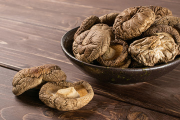 Lot of whole dry mushroom shiitake on grey ceramic plate on brown wood