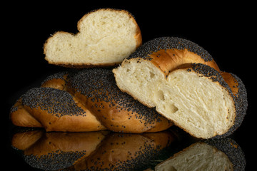 Group of one whole two halves of twisted poppy seed bun isolated on black glass