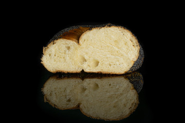 One half of twisted poppy seed bun isolated on black glass