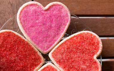 Obraz na płótnie Canvas Heart shaped sugar cookies with pink and red sprinkles on a plate