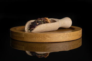 Lot of pieces of lingonberry strawberry fruit tea with wooden scoop on bamboo plate isolated on black glass