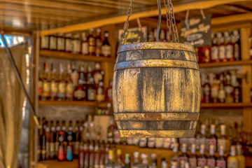 A whiskey barrel hangs in the foreground of a market stall. In the background are various drinks....
