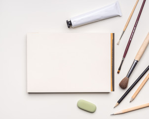 Blank page of notebook and scattered art tools on white background. Flat layout